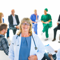 female doctor in the front with group of health professionals in a meeting behind her
